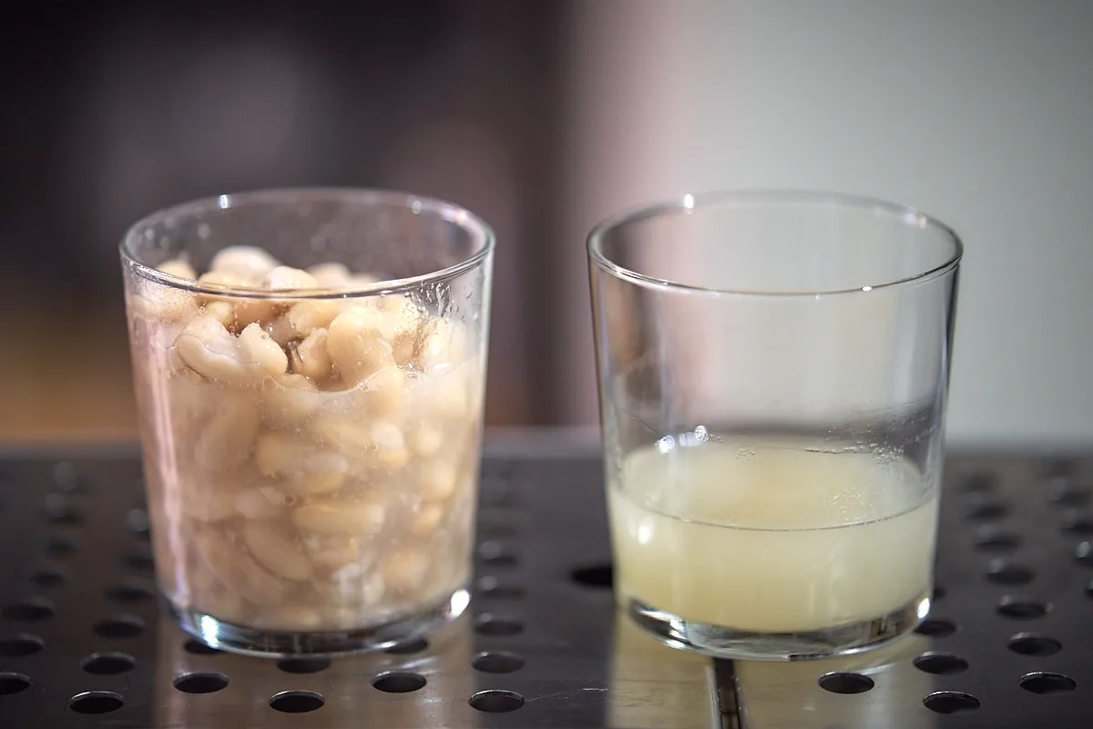 Bicchiere pieno di fagioli cannellini accanto a un bicchiere con poca acqua di cottura sul fondo
