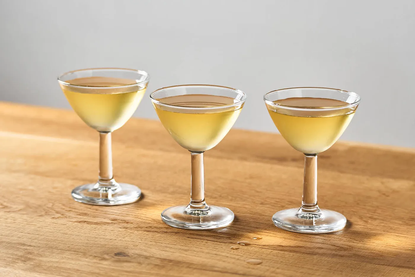 su un tavolo di legno 3 piccole coppette da cocktail contenenti 3 versioni di martini cocktail (secco, semisecco e morbido) bilanciati con Sorbole, bitter al limone.