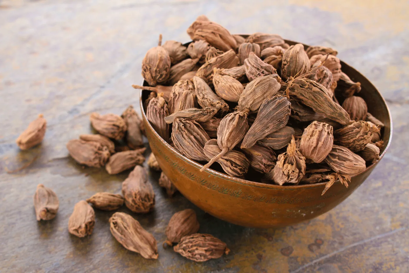 Una ciotola di rame piena di capsule marroni e rugose di cardamomo nero, più grandi di quelle verdi