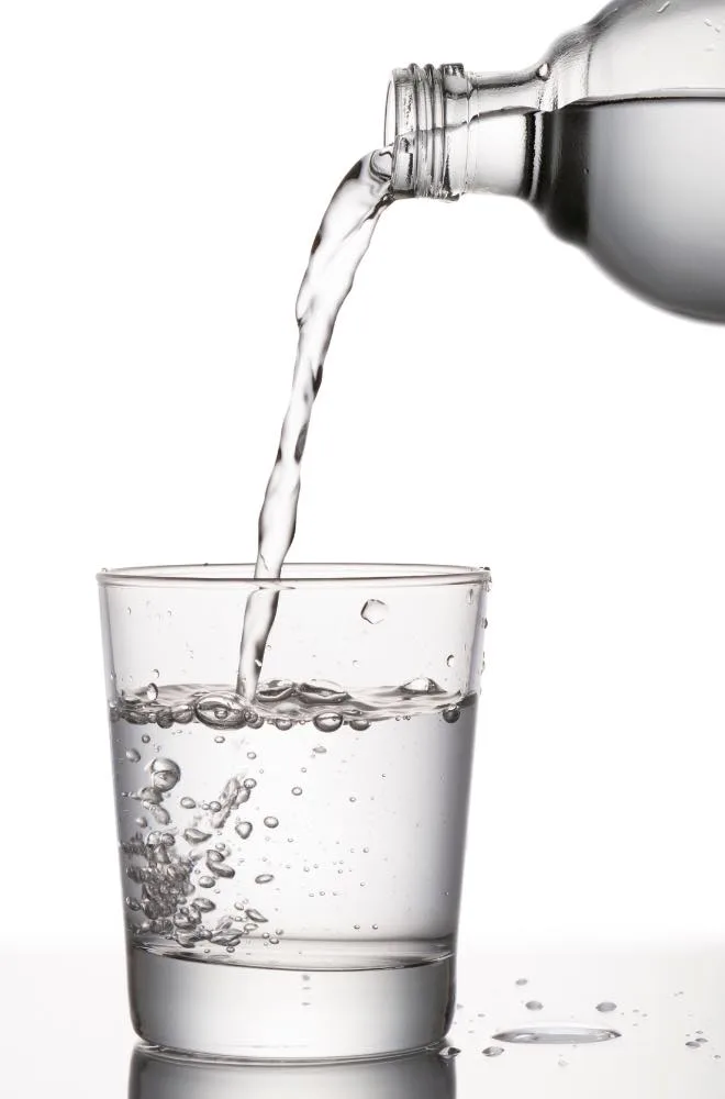 Acqua versata da una bottiglia in un bicchiere: un liquido incolore, senza alcun colore proprio