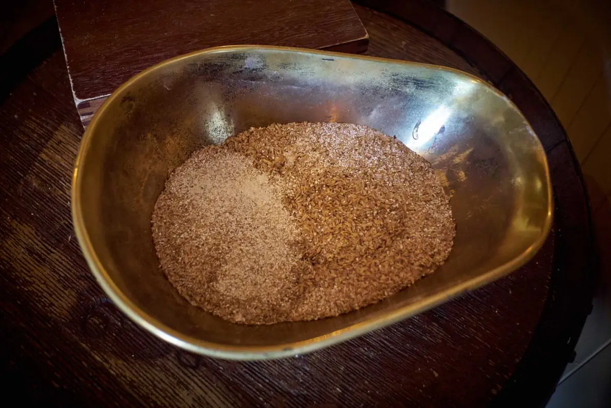 Grist, orzo maltato macinato grossolanamente, in una ciotola di ottone appoggiata su una botte