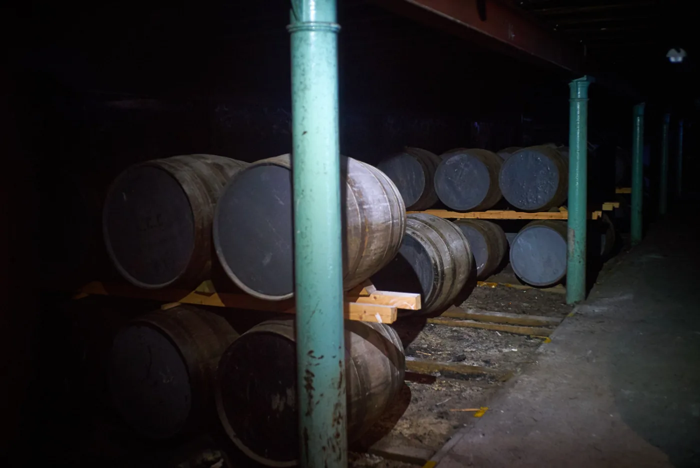 Botti di whisky accatastate su travi di legno in un magazzino buio con colonne verdi