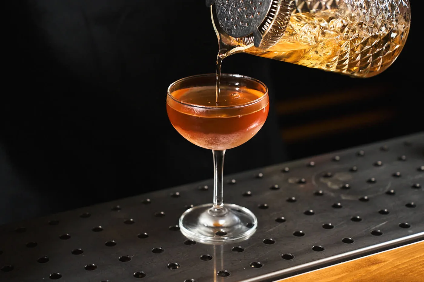 Su un banco bar, il cocktail El Presidente che viene versato da un mixing glass all'interno di una coppetta.