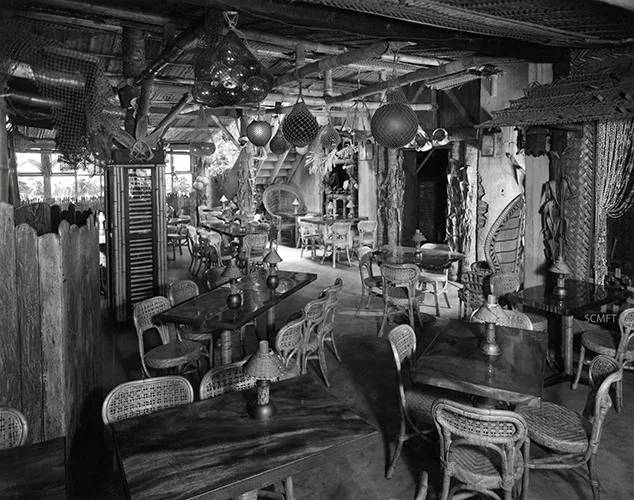 Fotografia in bianco e nero della sala del Don the Beachcomber: tavoli, sedie di vimini, reti, galleggianti e lanterne appesi al soffitto