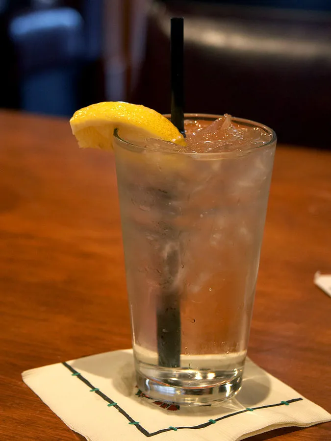Long drink servito in un tumbler alto riempito di ghiaccio fino all’orlo, con spicchio di limone e cannuccia nera