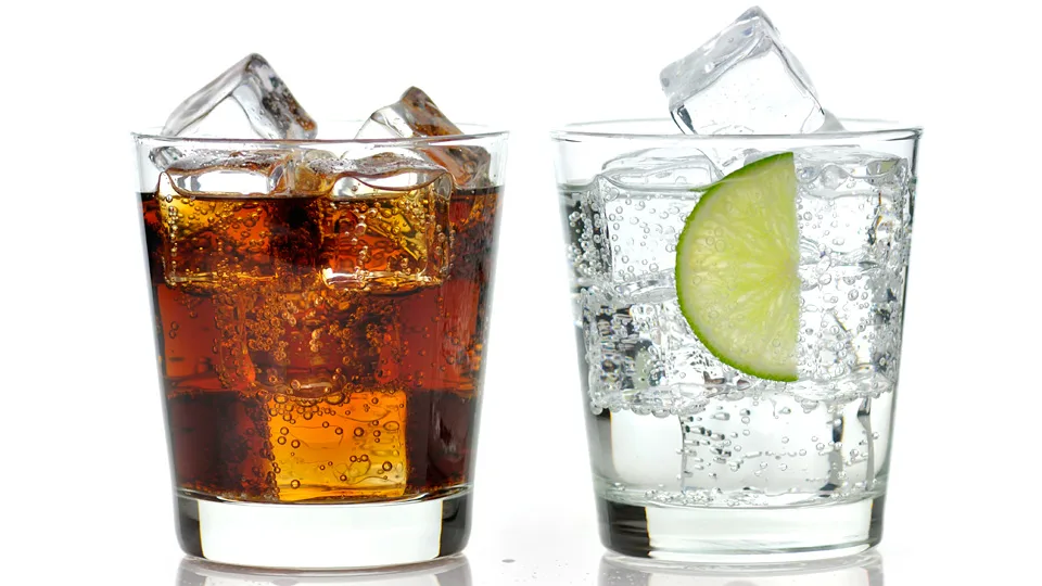 Due tumbler bassi riempiti di ghiaccio fino all’orlo, uno con un drink scuro alla cola e uno con soda e una fetta di lime