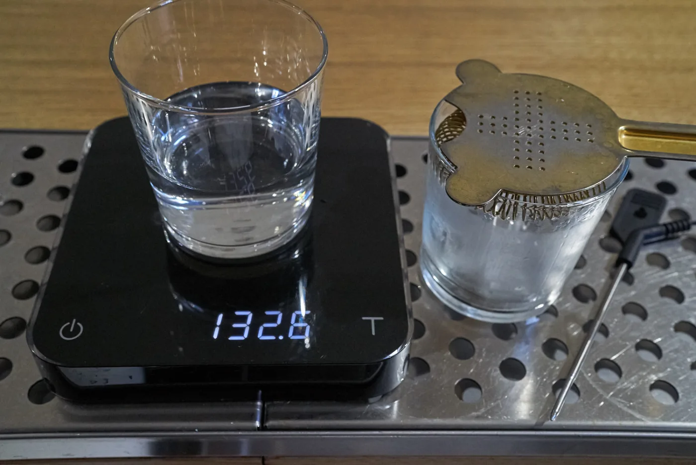 Bilancia digitale che segna 132,6 grammi accanto al mixing glass con i 3 cubetti residui e lo strainer