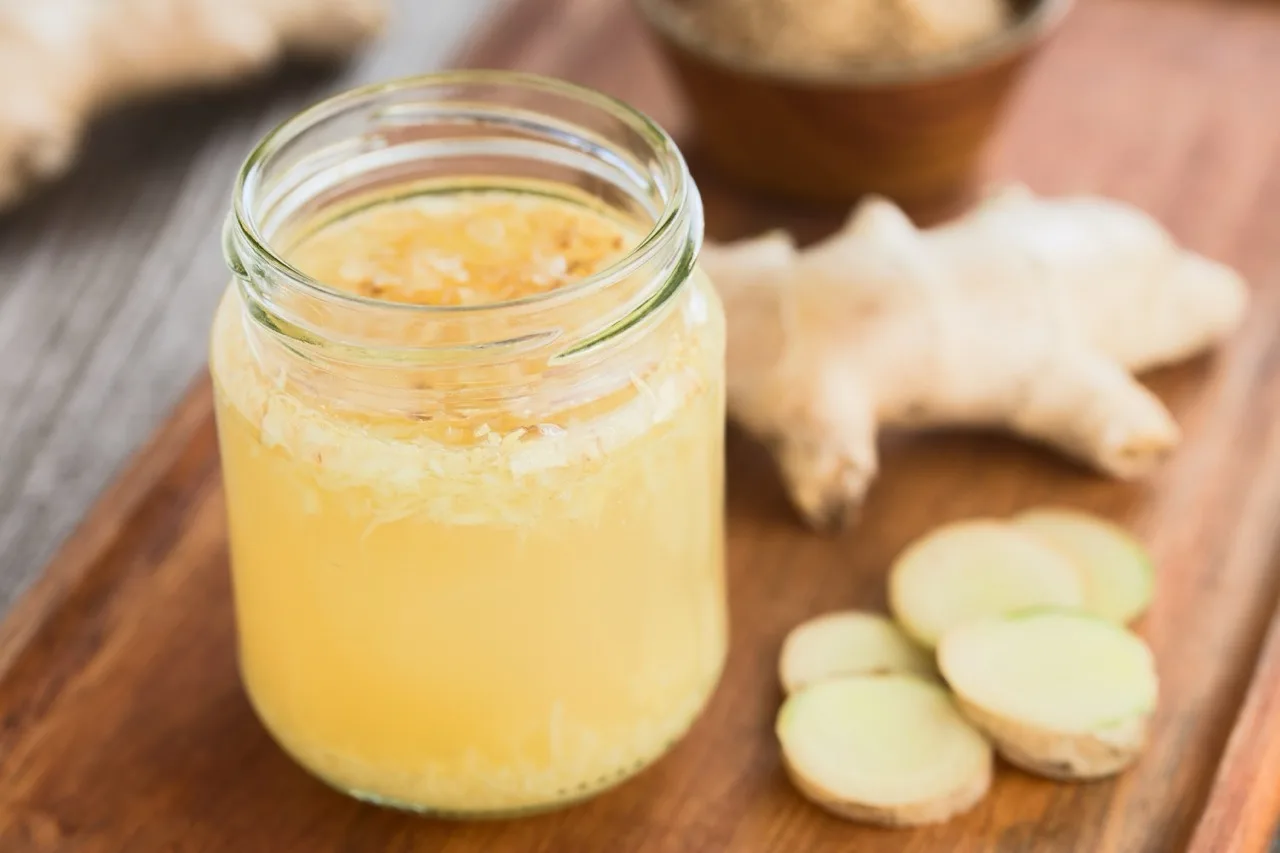 Barattolo di vetro con ginger bug torbido e zenzero grattugiato in superficie, accanto a radice e fette di zenzero