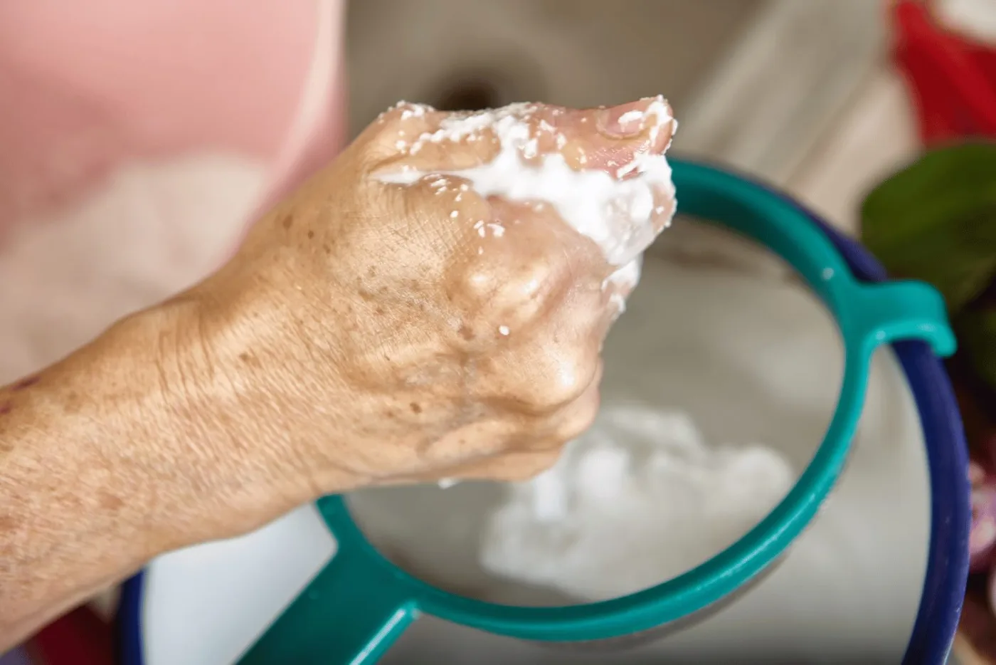 Una mano strizza la polpa di cocco grattugiata sopra un colino per estrarre il latte di cocco