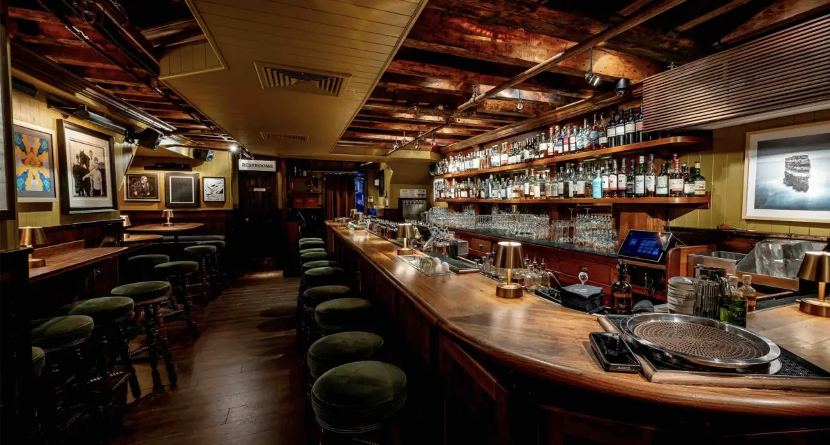 L'interno in legno del Dead Rabbit di New York, con il lungo bancone, gli sgabelli verdi e le bottiglie sugli scaffali