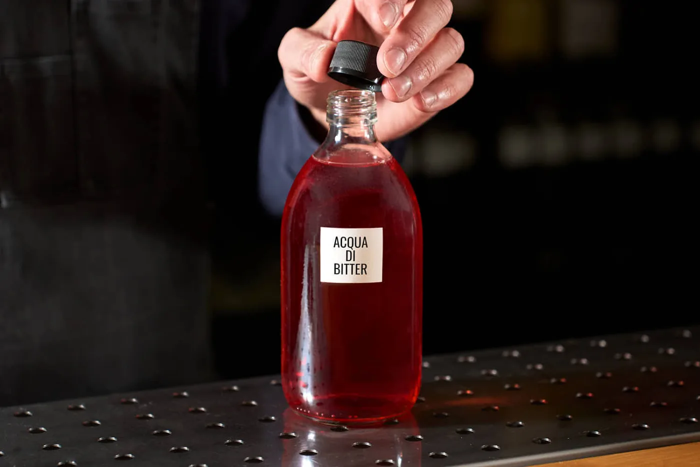 Su un banco bar sun bottiglia contente una preparazione home made chiamata acqua di bitter. La preparazione viene utilizzata nel cocktail "Italoma" ed è composta da bitter classico, acqua, zuccher e acido citrico.