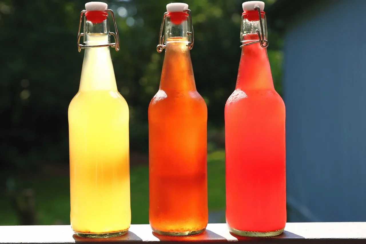 Tre bottiglie con tappo meccanico di cocktail analcolici prebatch a base kombucha e frutta, di colore giallo, ambrato e rosso
