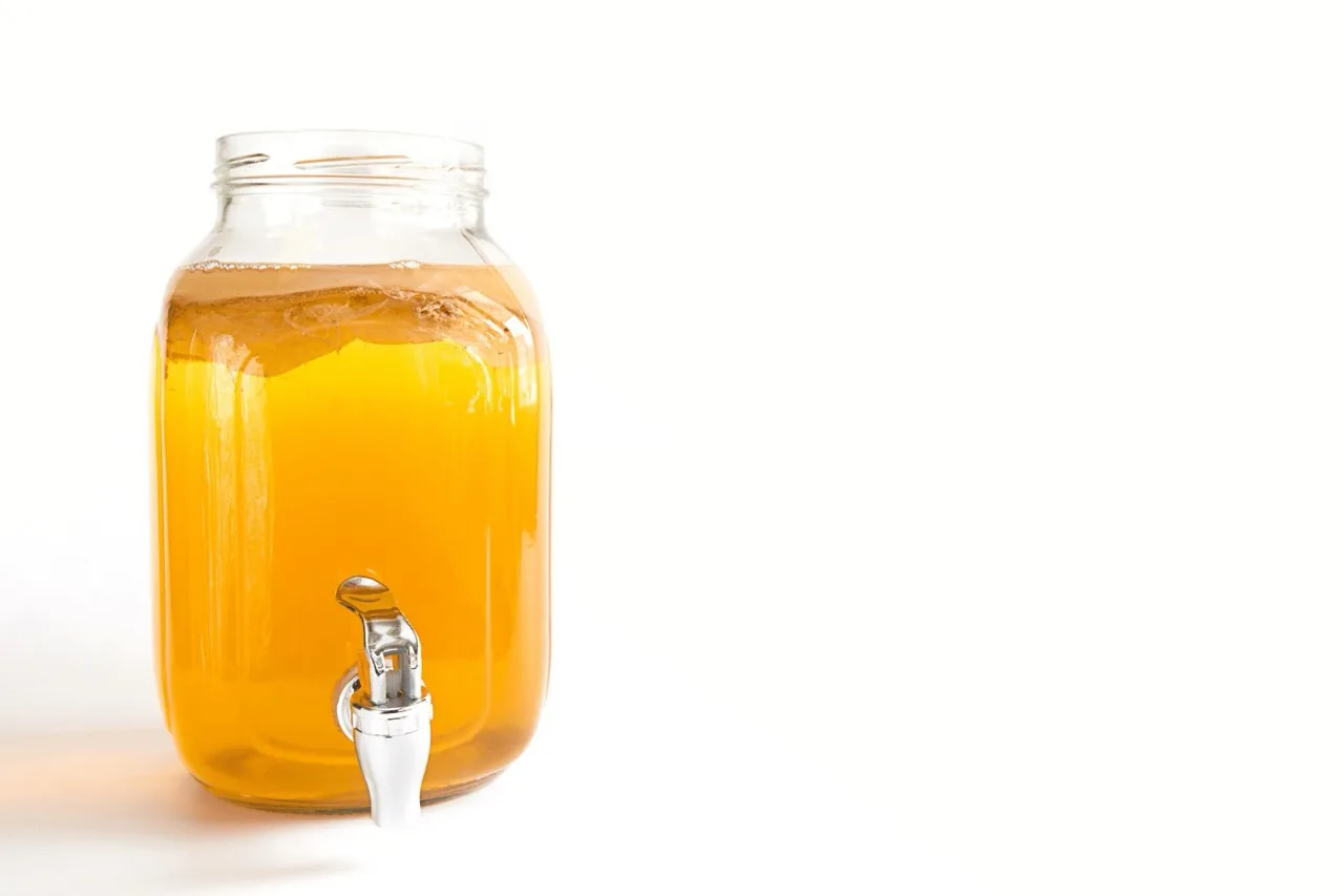 Barattolo di vetro con rubinetto pieno di kombucha con SCOBY in superficie