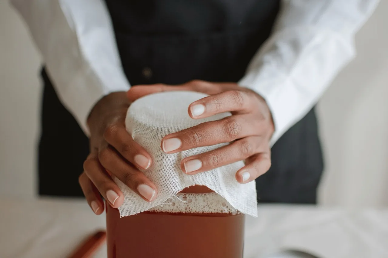 Mani che fissano un canovaccio traspirante sul barattolo di kombucha in fermentazione