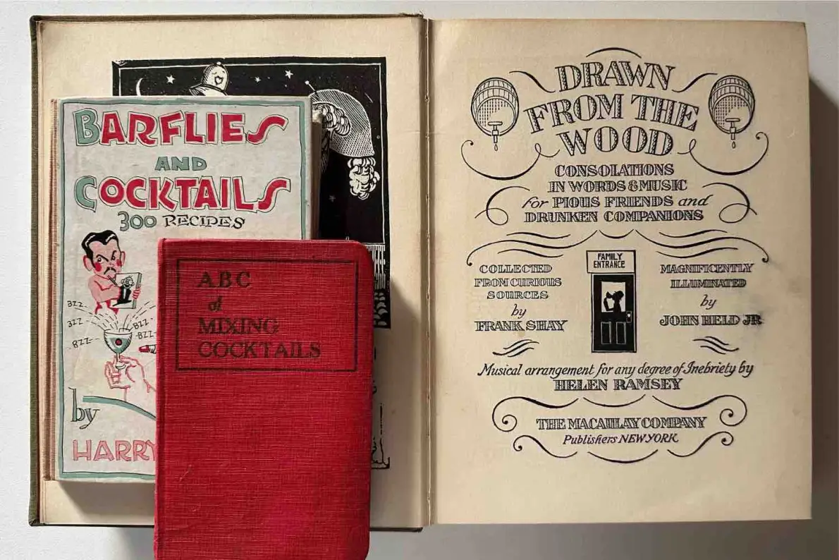 Tre libri storici: Barflies and Cocktails di Harry MacElhone, la copia rossa di ABC of Mixing Cocktails e il frontespizio di Drawn from the Wood di Frank Shay