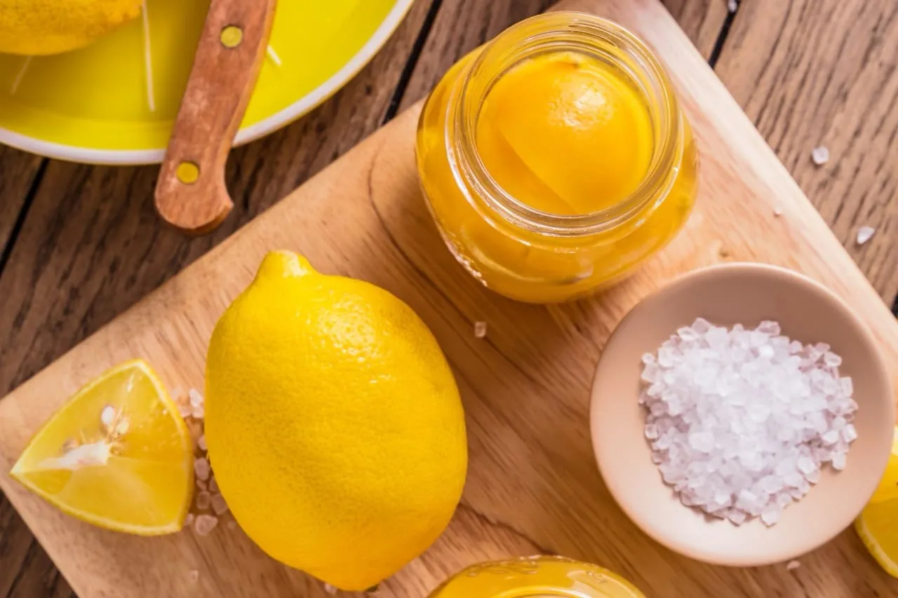 Limoni freschi, barattolo di limoni sotto sale e ciotolina di sale grosso su un tagliere di legno