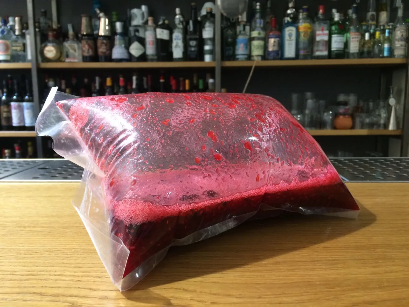 Sacchetto sottovuoto gonfio contenente un liquido rosso in fermentazione, con schiuma e bollicine