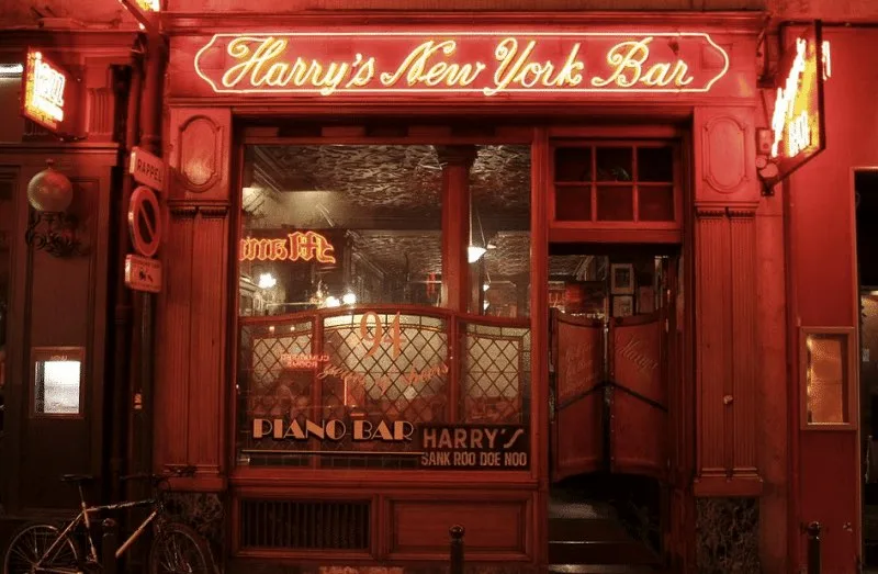 La facciata dell'Harry's New York Bar di Parigi di notte, con l'insegna rossa illuminata e la scritta Sank Roo Doe Noo
