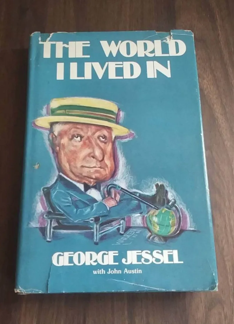 Copertina azzurra del libro The World I Lived In di George Jessel con la caricatura dell'autore in paglietta e un mappamondo