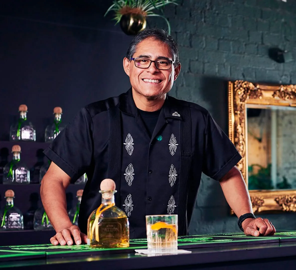 Julio Bermejo sorridente dietro al bancone con bottiglie di tequila e un Tommy's Margarita
