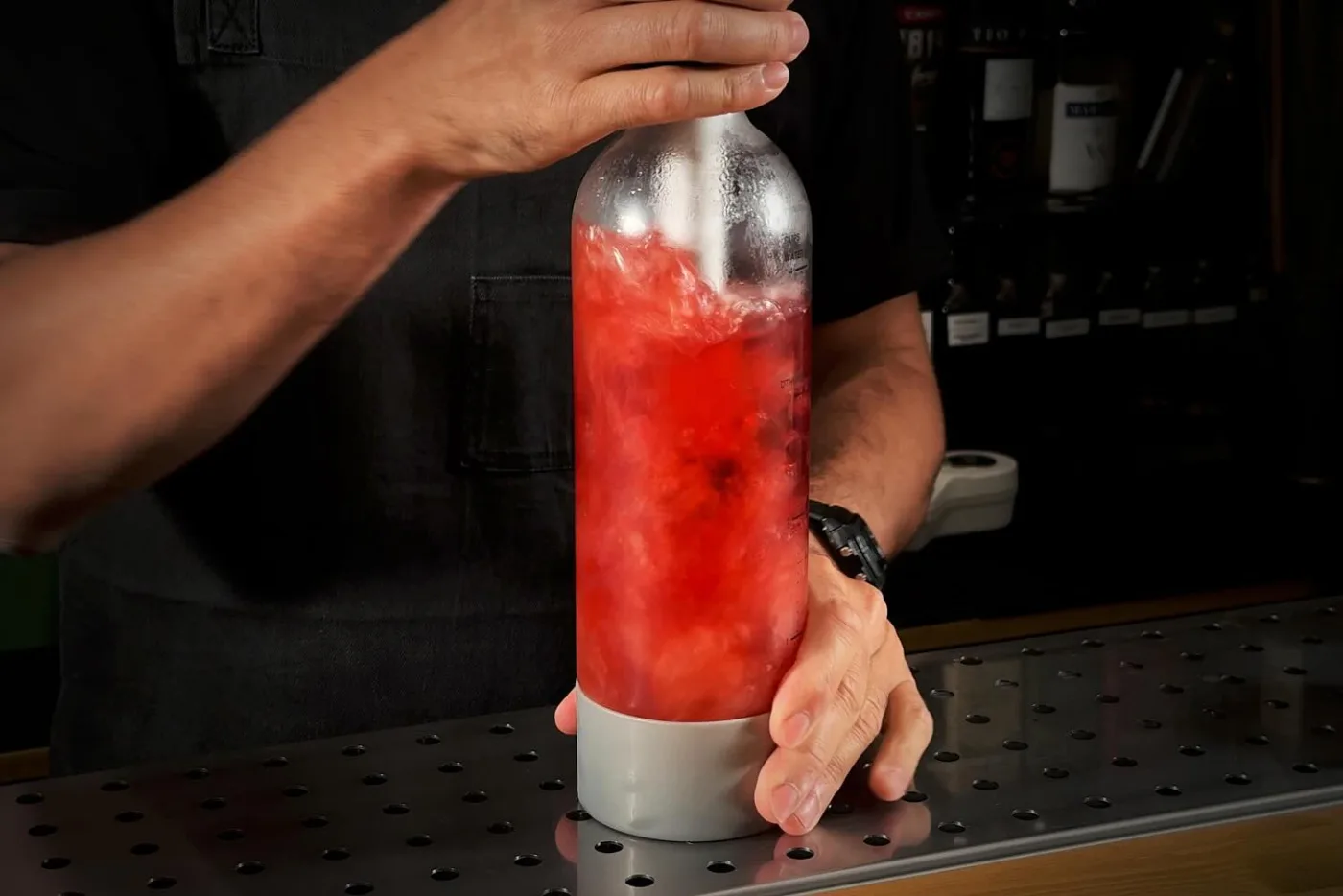 Bartender che gassa la tonica all'açai rossa in una bottiglia Twist'n Sparkle sul banco bar
