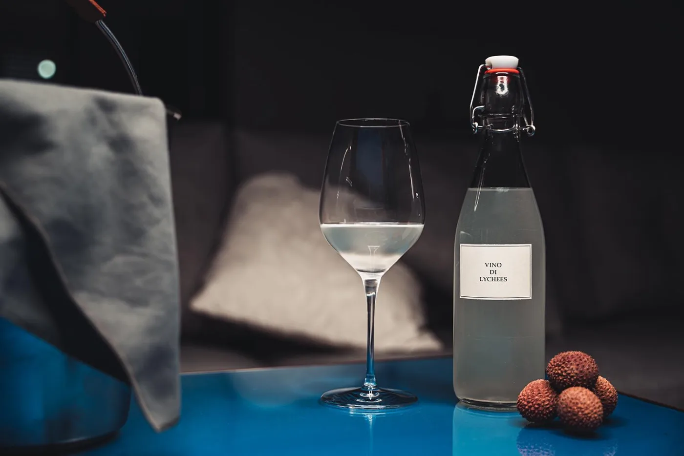 Bottiglia etichettata Vino di Lychees accanto a un calice e a dei litchi freschi