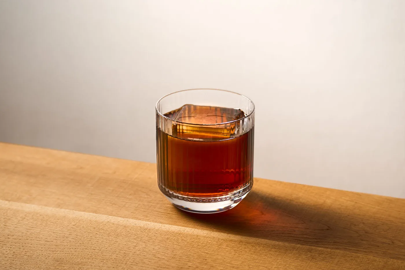 su un tavolo in legno il cocktail black russian preparato con Vodka e liquore al caffè. Il cocktail è servito in un tumbler basso rigato con chunk di ghiaccio